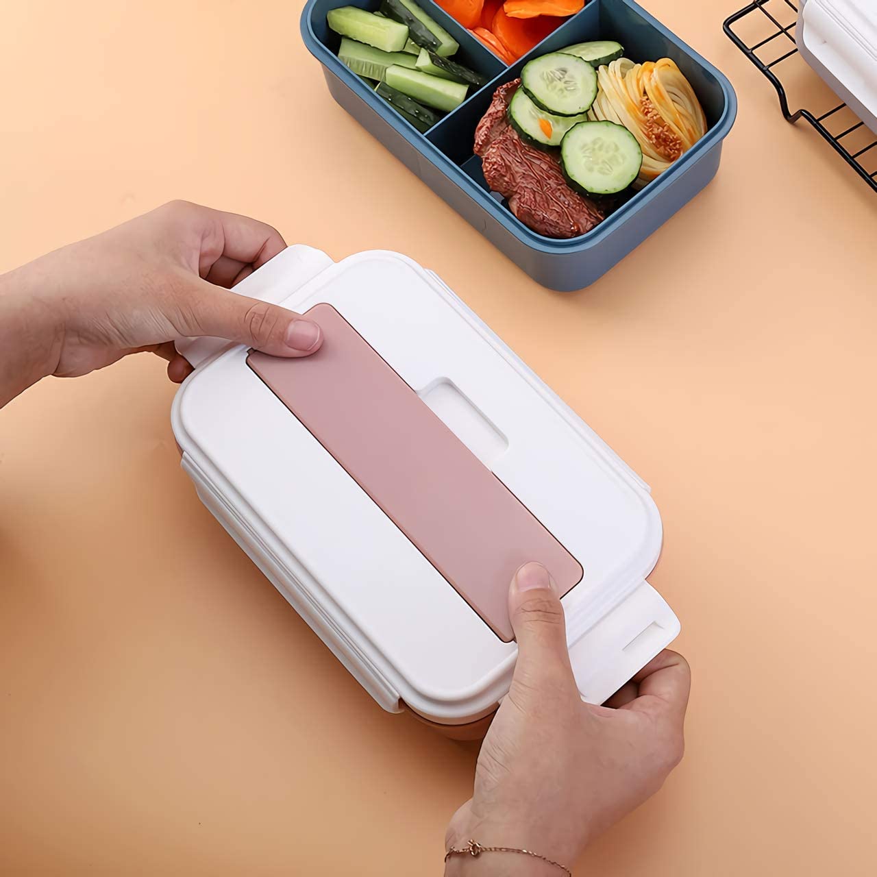 Person opening a white lunch box with a pink interior, containing a bento-style meal.
