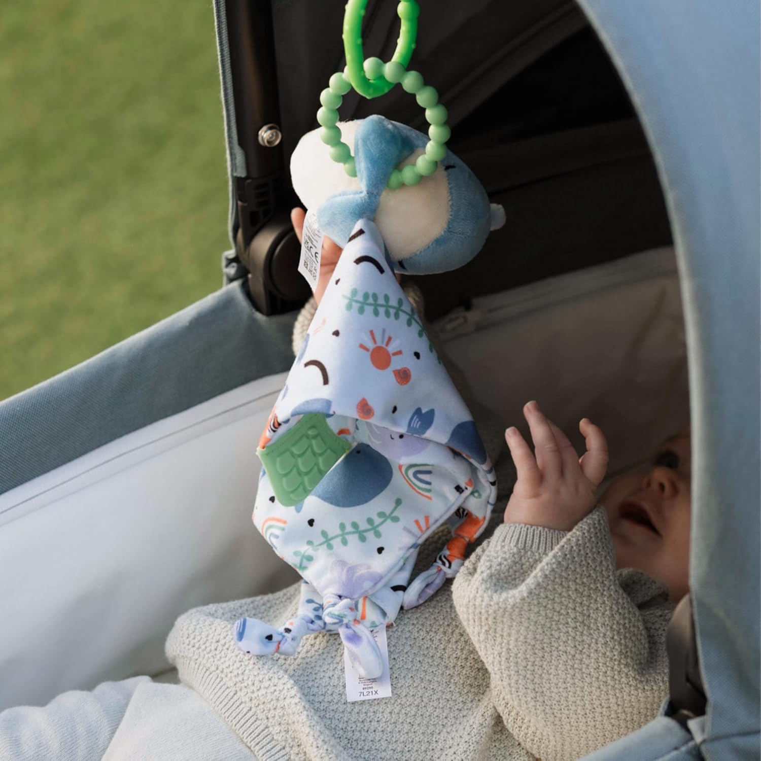 Baby playing with a colorful mobile toy hanging from a stroller.